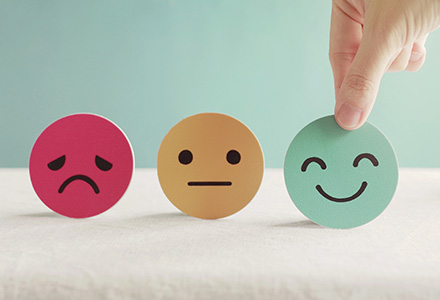 Hand holding circles with faces on them: sad, neutral, and happy